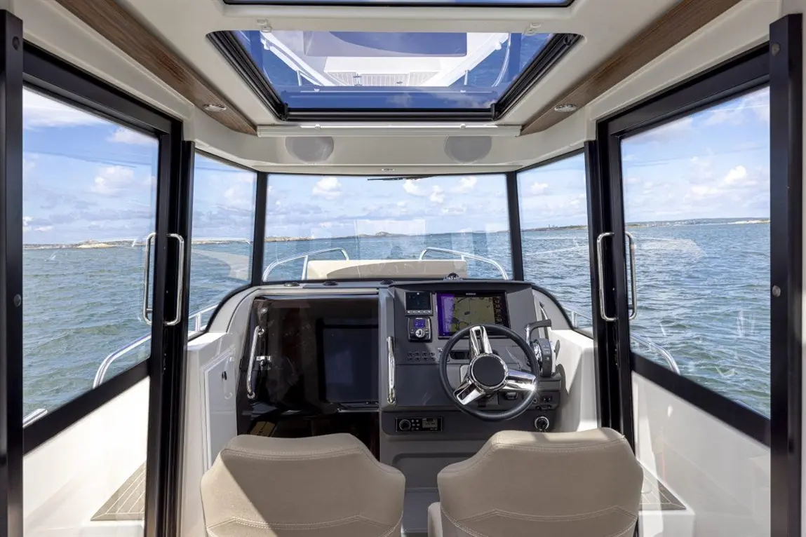 Interior view of a boat's helm, featuring a steering wheel, touch screen, and panoramic windows overlooking the water.
